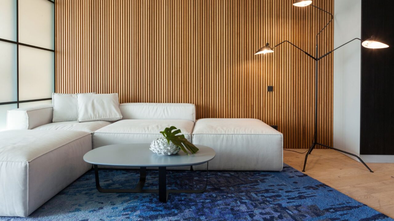 A living room interior with a white sofa, coffee table, floor lamp, and a blue rug.