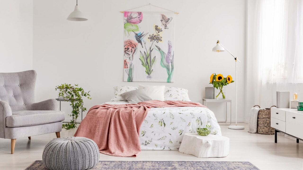 A stylish bedroom with a cozy bed with throw blanket, armchair, flowers, and artwork on the wall.