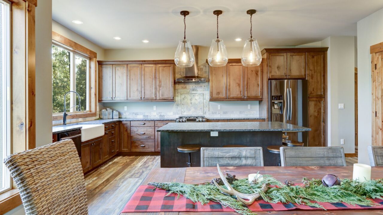 A rustic kitchen interior with reclaimed wood cabinetry, dining table, and cozy pendant lighting.