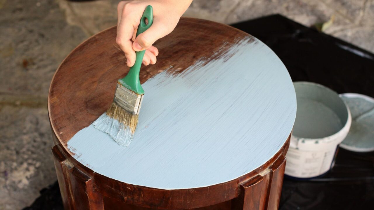 A person painting a wooden table with white paint.