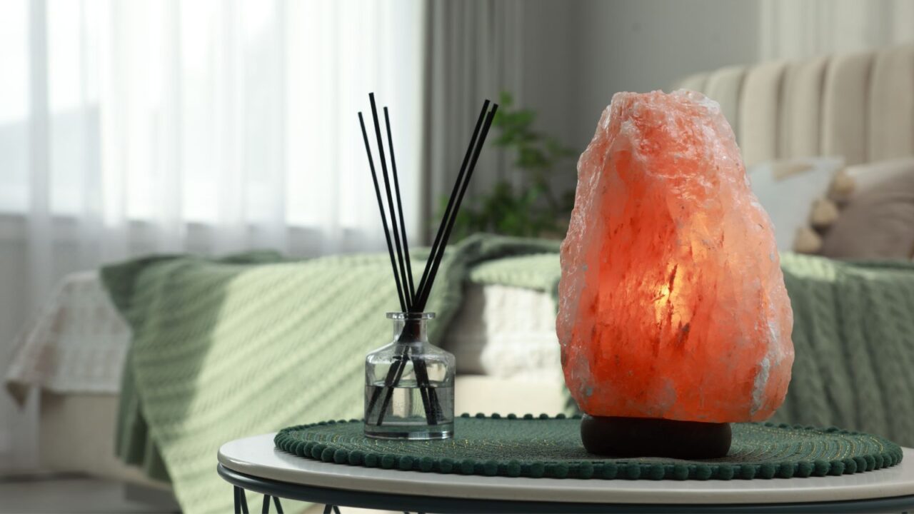 A reed diffuser and Himalayan salt lamp on a table in a bedroom.