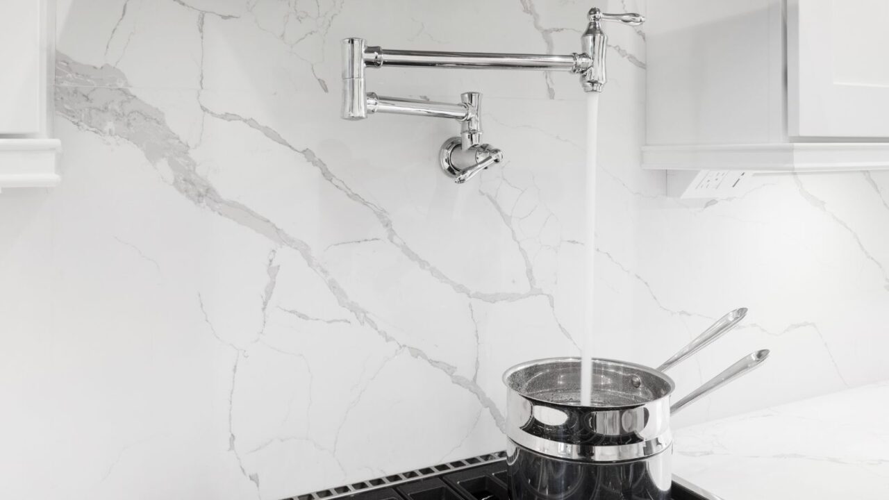 A granite backsplash with a pot filler faucet and a pot on the stove.