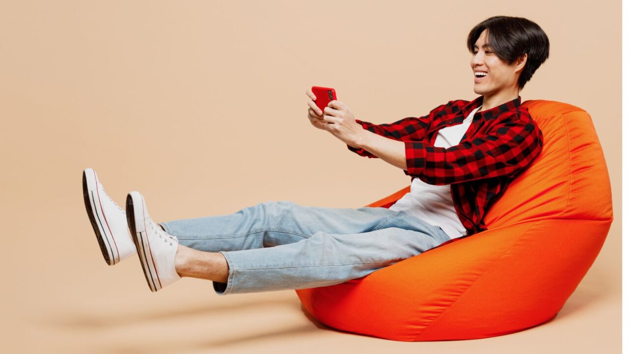 A man sitting on an orange bean bag chair on a beige background.