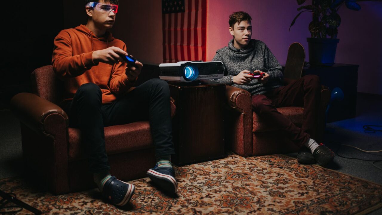 An entertainment room with cozy sofas, rugs, projector, and people playing videogames.