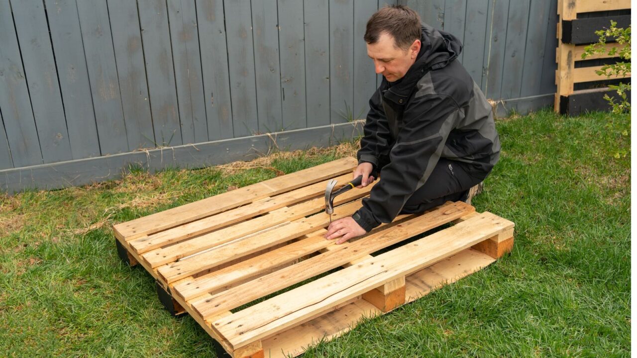 A man hammering a nail in the wooden pallet.