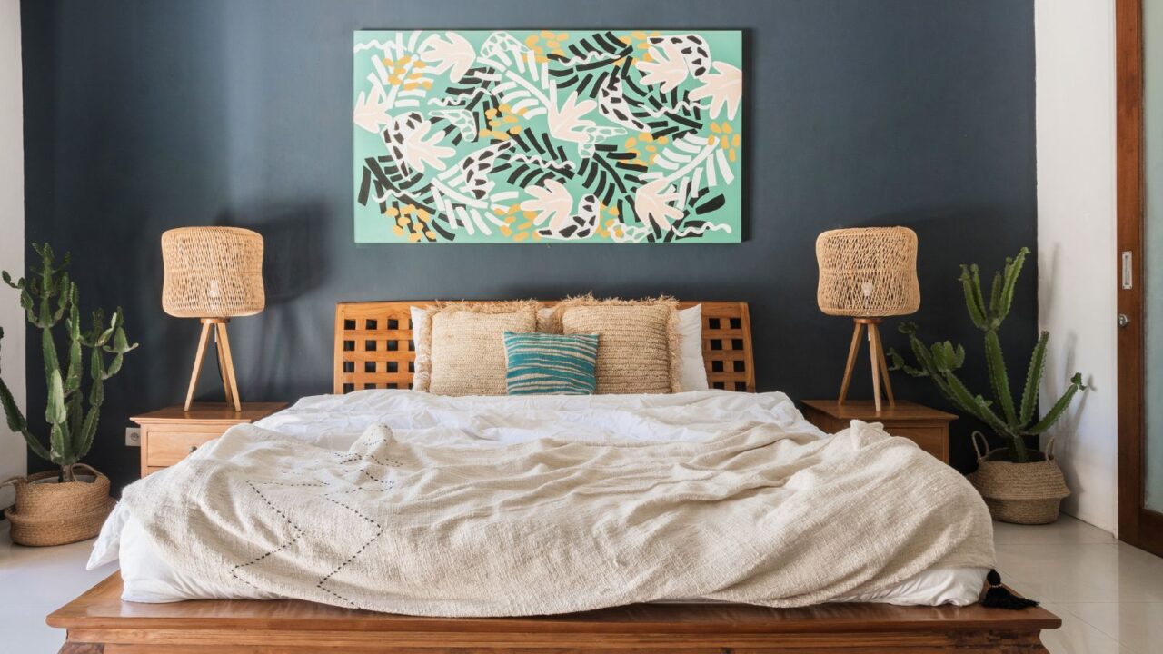 A bedroom interior with a wooden bed, lamps, houseplants, and an oversized painting above bed.