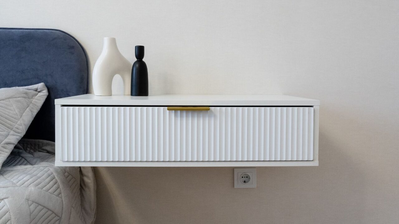 A sleek white floating nightstand with sculpted vases on it.