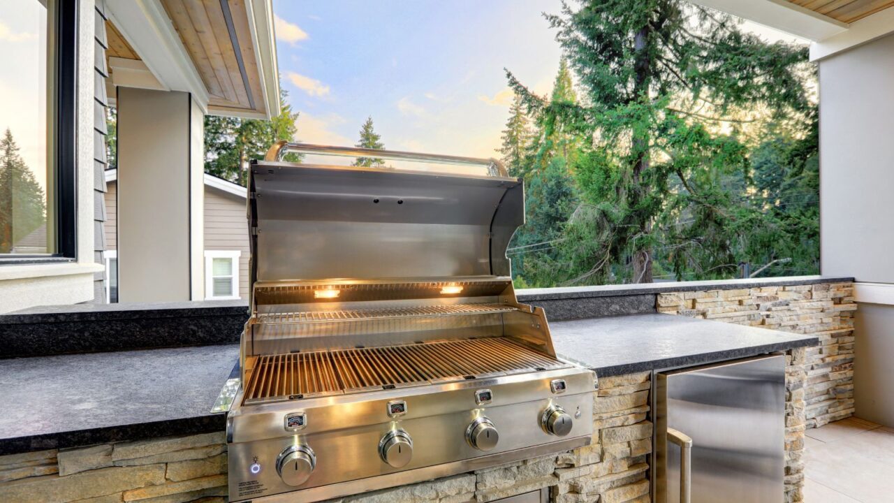 A stainless steel grill and built-in refrigerator in an outdoor kitchen on the patio.