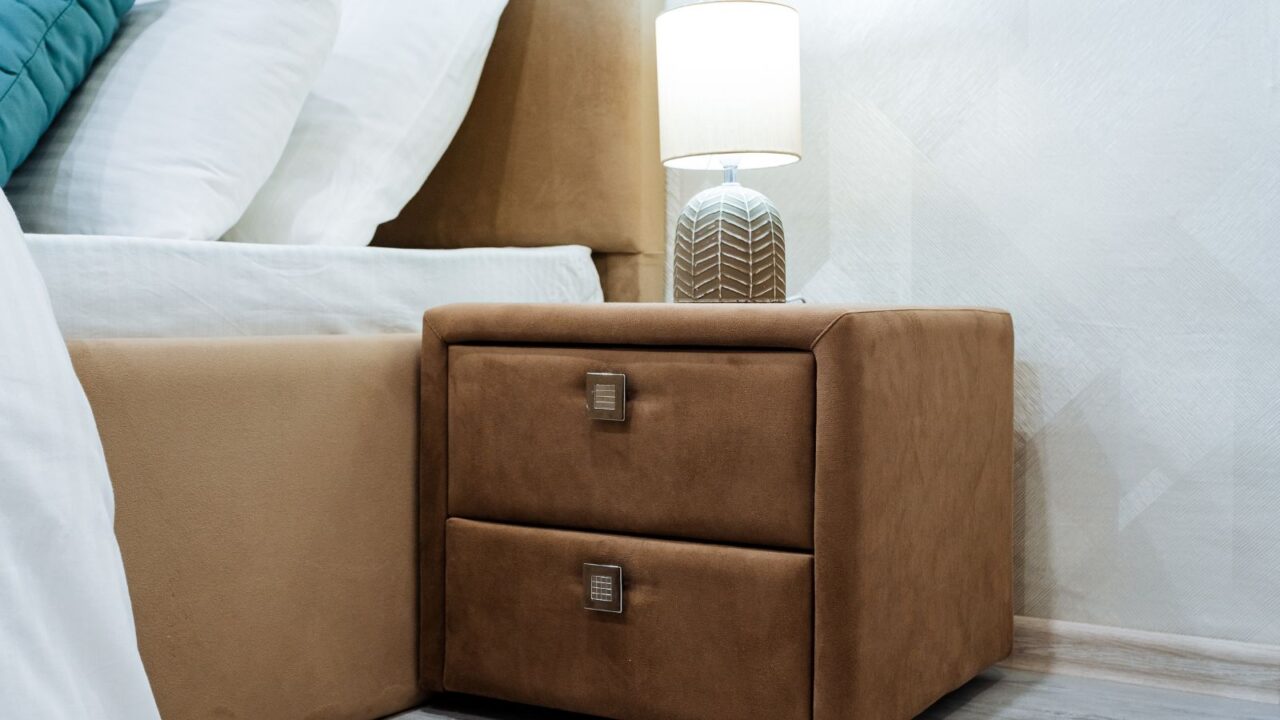 An upholstered soft finish brown nightstand with lamp on it.