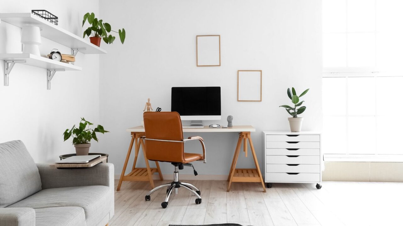 A minimalist workspace with a computer, a brown chair, and potted plants in a bright room.