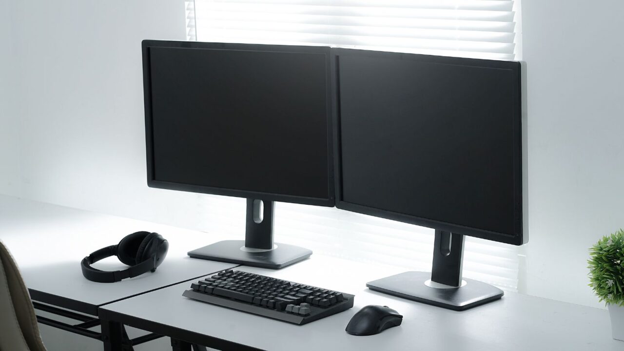 A workspace with dual computers, keyboard, mouse, and headphones on a white table.