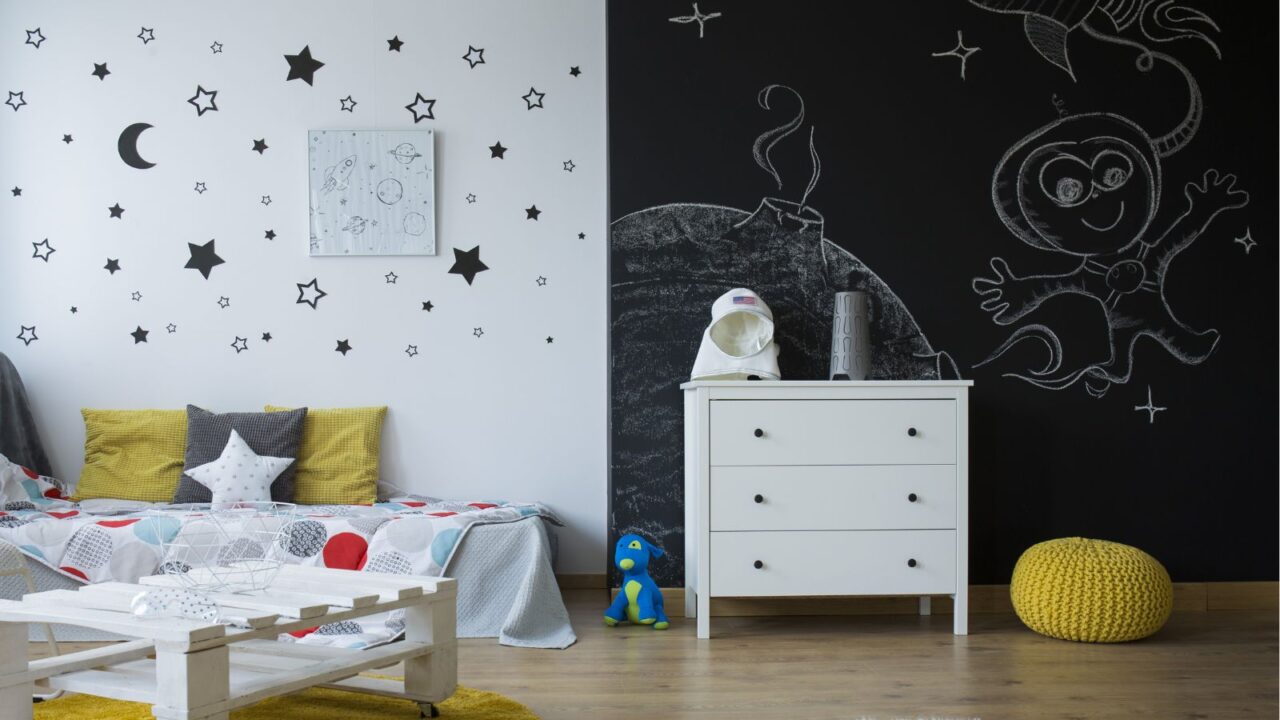 A bedroom interior with a mattress with pillows, floor cushion, and a chalkboard wall.