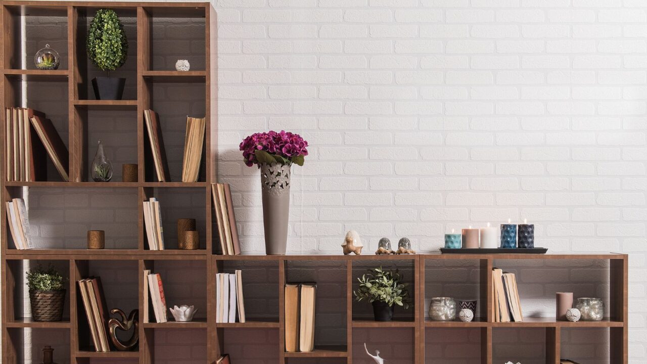 A wooden bookshelf with books, plants, decor accents, and candles in front of a white wall.