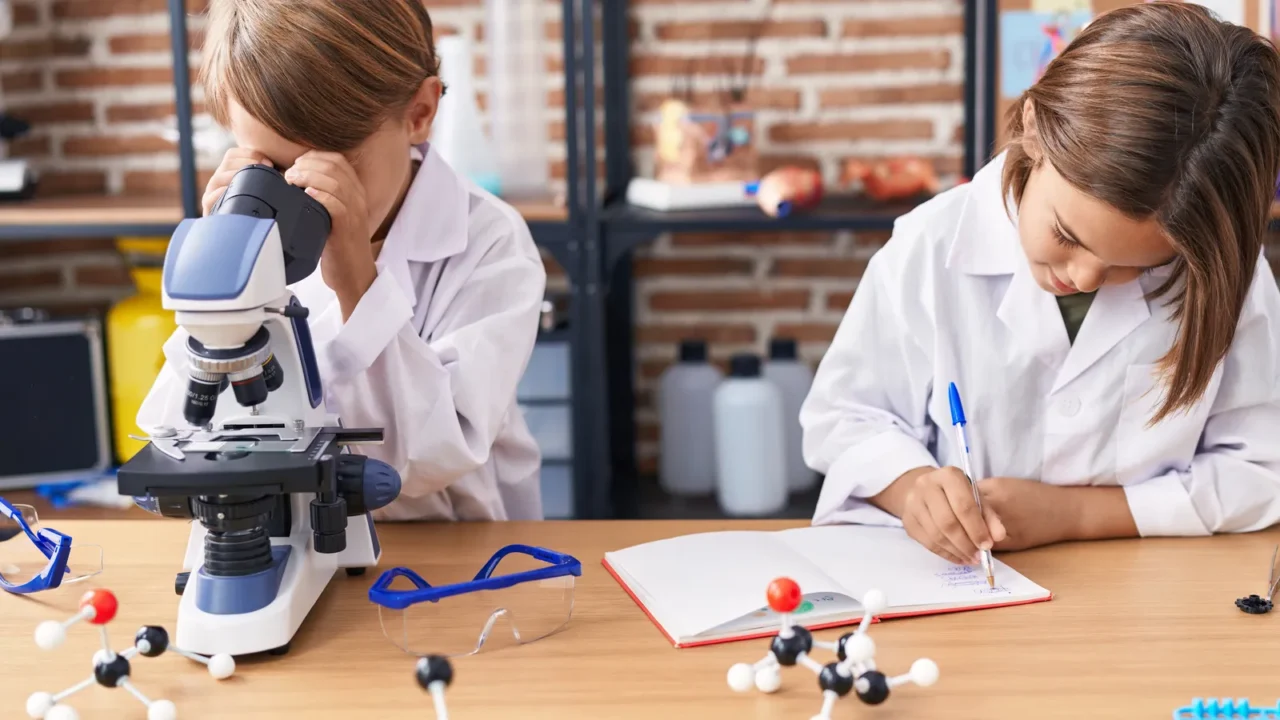 adorable boys students using microscope writing notes at laboratory classroom