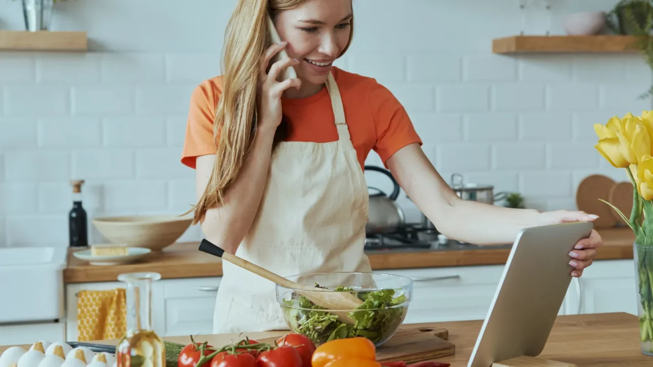 beautiful young woman talking on mobile phone while cooking at