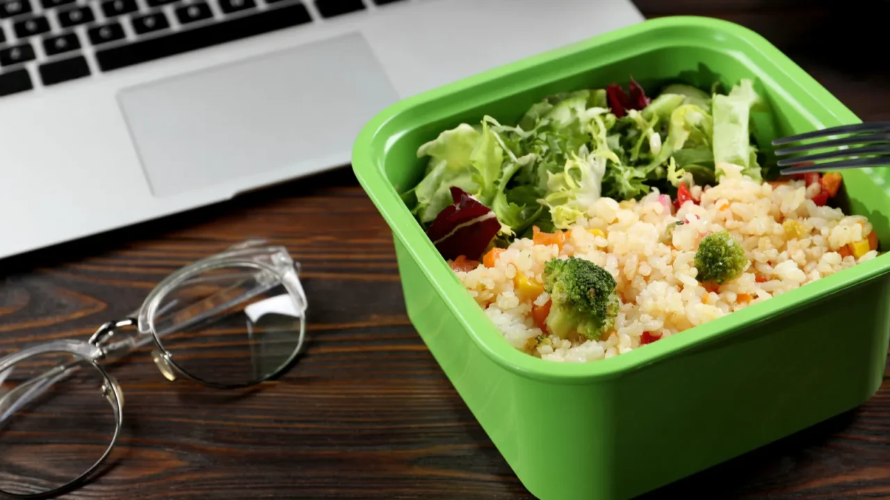 container with tasty food fork laptop and glasses on wooden