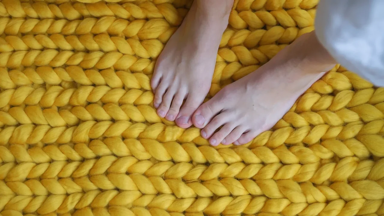 A woman standing on a yellow chunky knit rug.