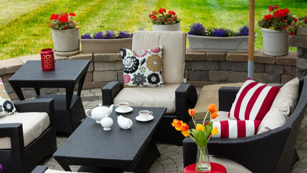 Floral and striped throw pillows on sofas in a patio with flower pots on its edges.