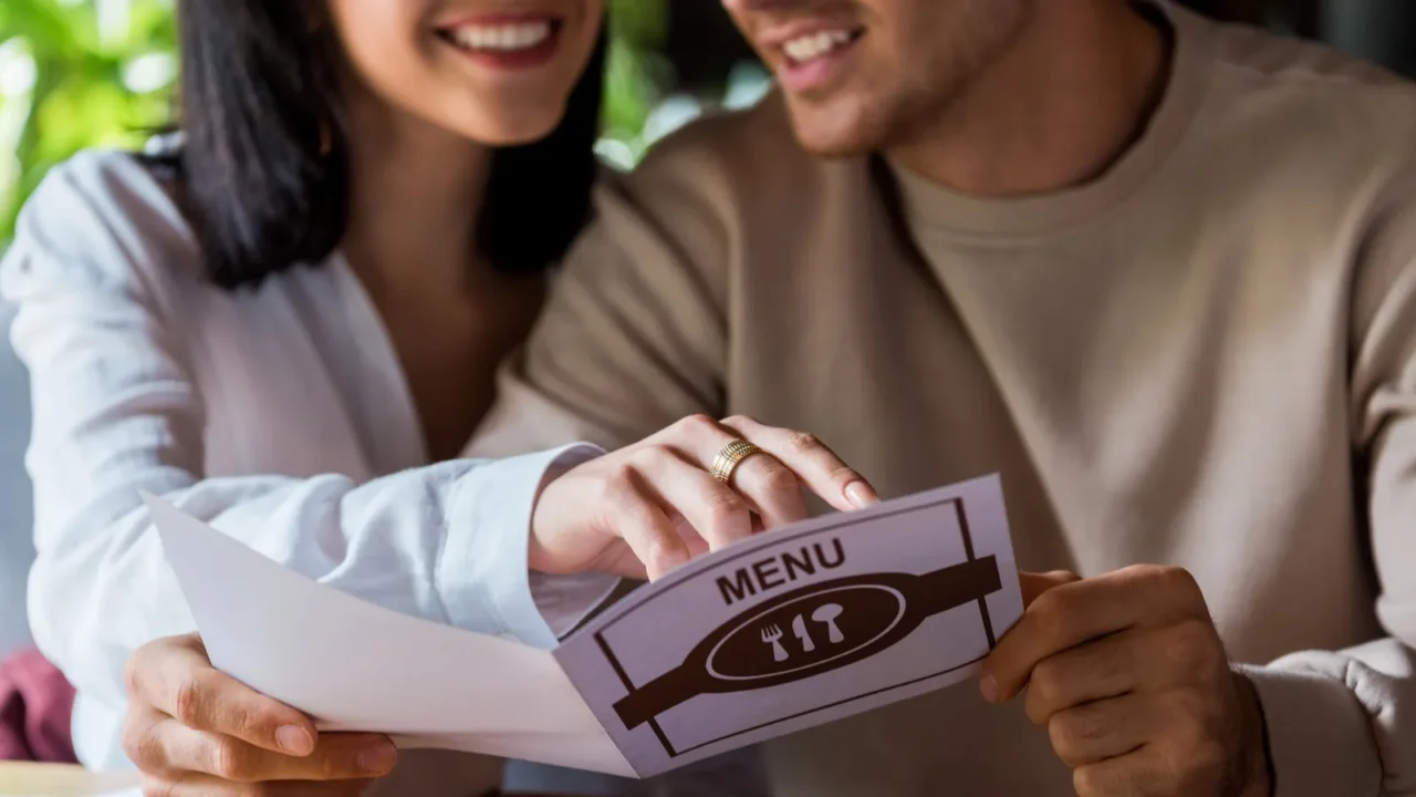 A couple smiling and reviewing a restaurant menu together.