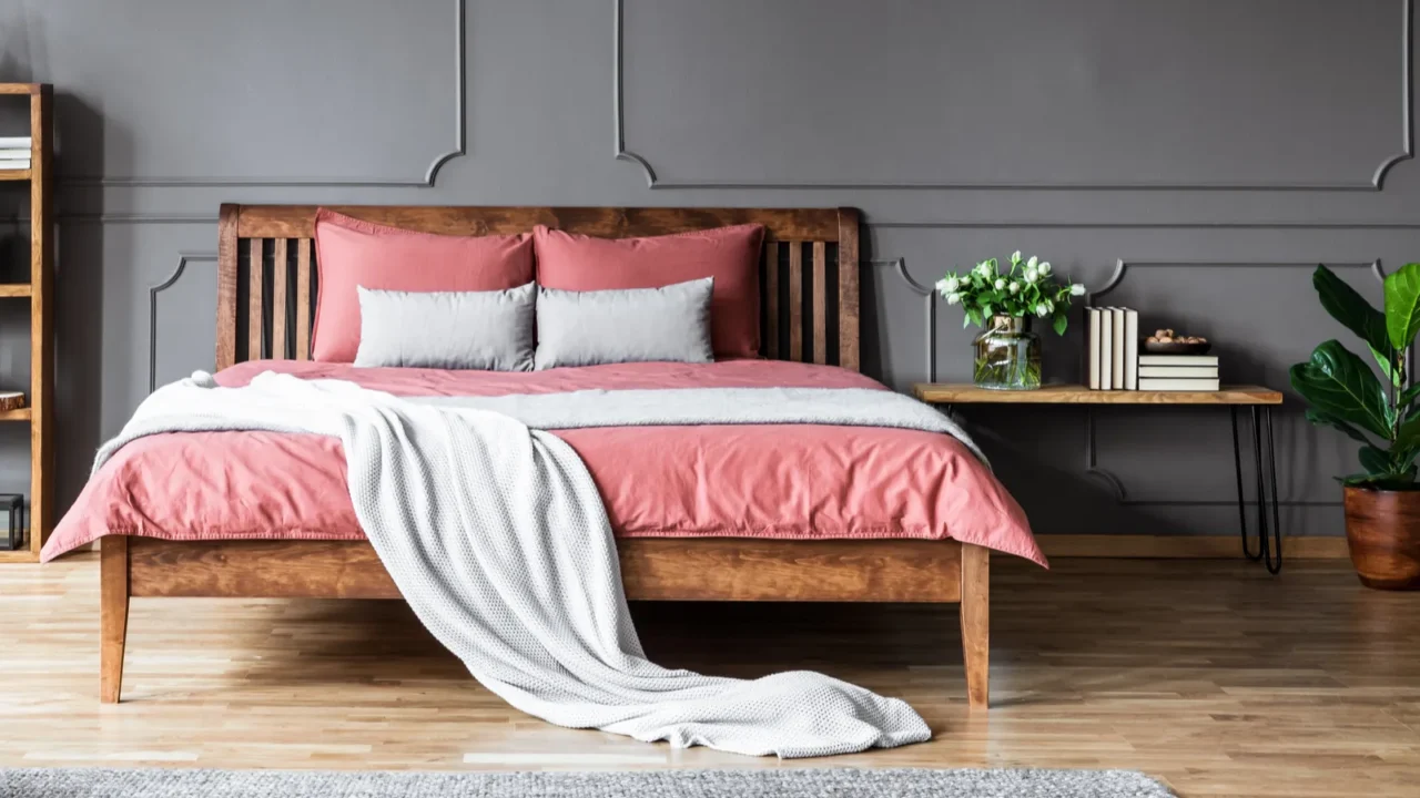 A cozy bedroom interior with coral bedding, pillows, cushions, and throw blanket on a wooden bed, rug, and wooden side table.