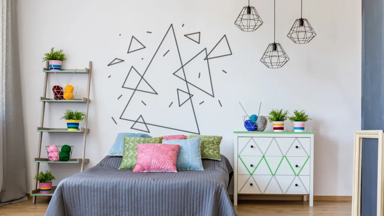 A bedroom interior with a cozy bed with pillows, a ladder shelf, bedside table, plants, pendant lights, and washi tape art on the wall.