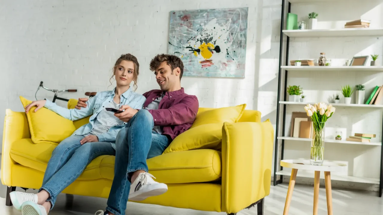 happy man and young woman watching movie while robotic vacuum