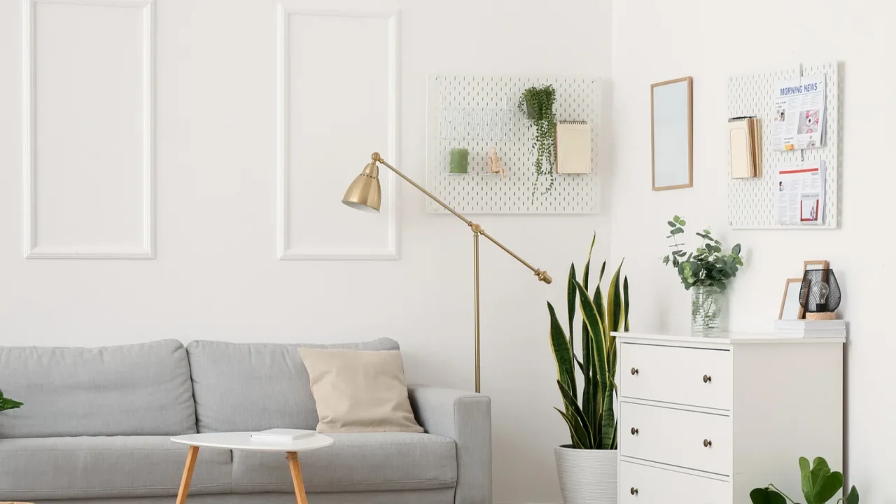 A living room interior with sofa, floor lamp, coffee table, console table, and pegboards hanging on the wall.