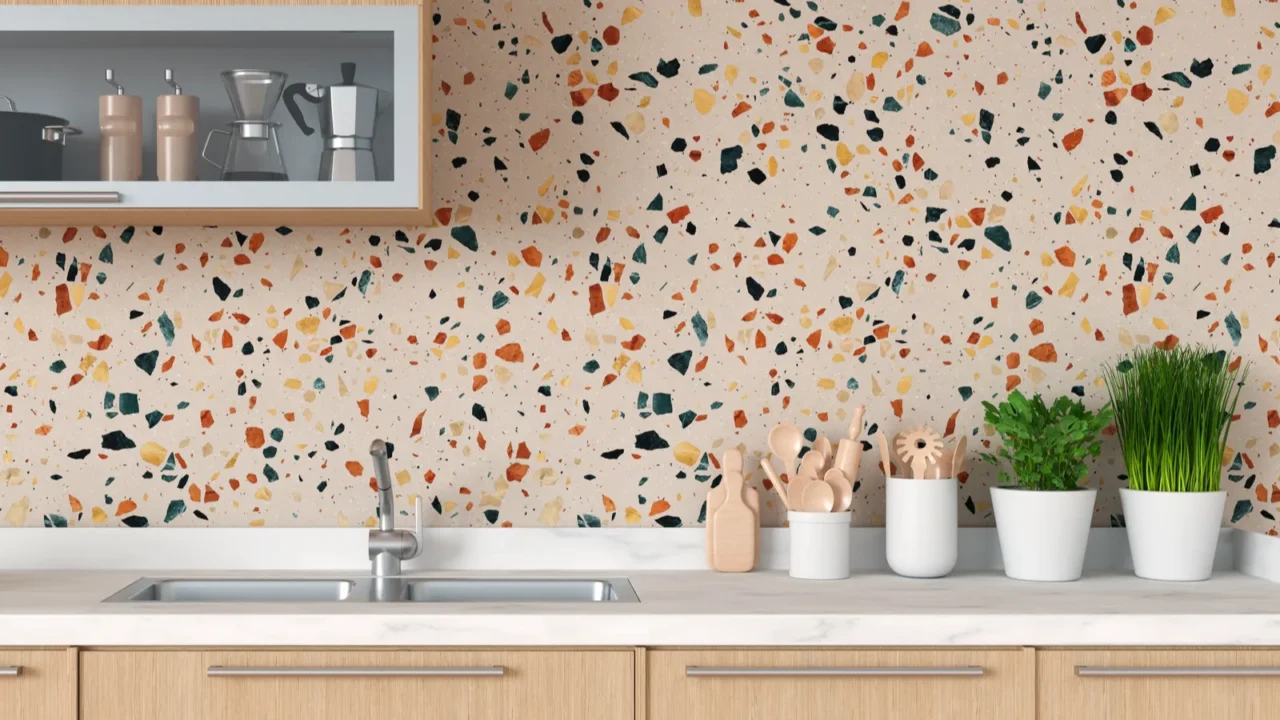 A kitchen showcasing a colorful terrazzo wall behind a white sink and natural wood cabinetry.