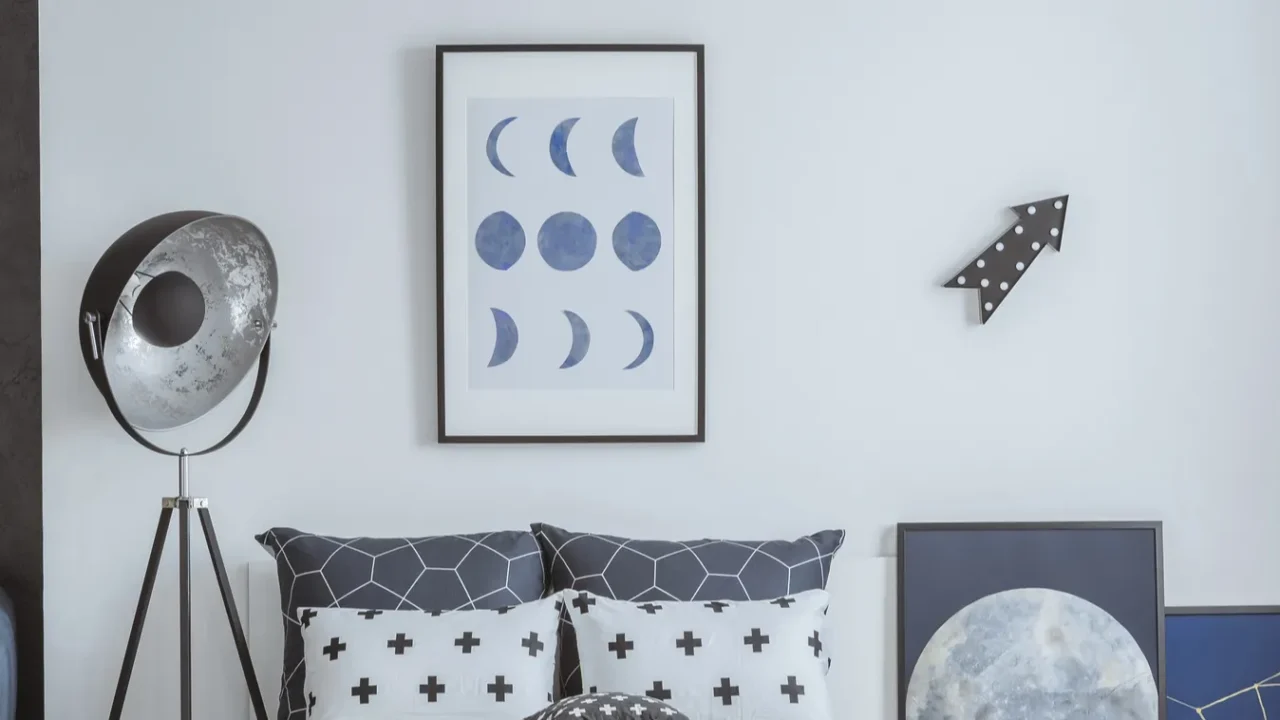 A moon-themed periwinkle blue bedroom interior with floor lamp, blue and white cushions, and framed moon poster on the wall.