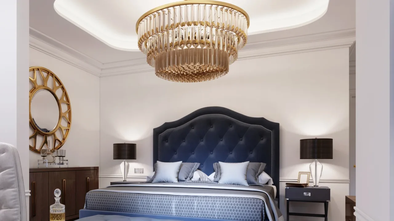 A luxurious bedroom interior with cozy bed with curved upholstered headboard, bedside table with lamp, and chandelier hanging from the ceiling.