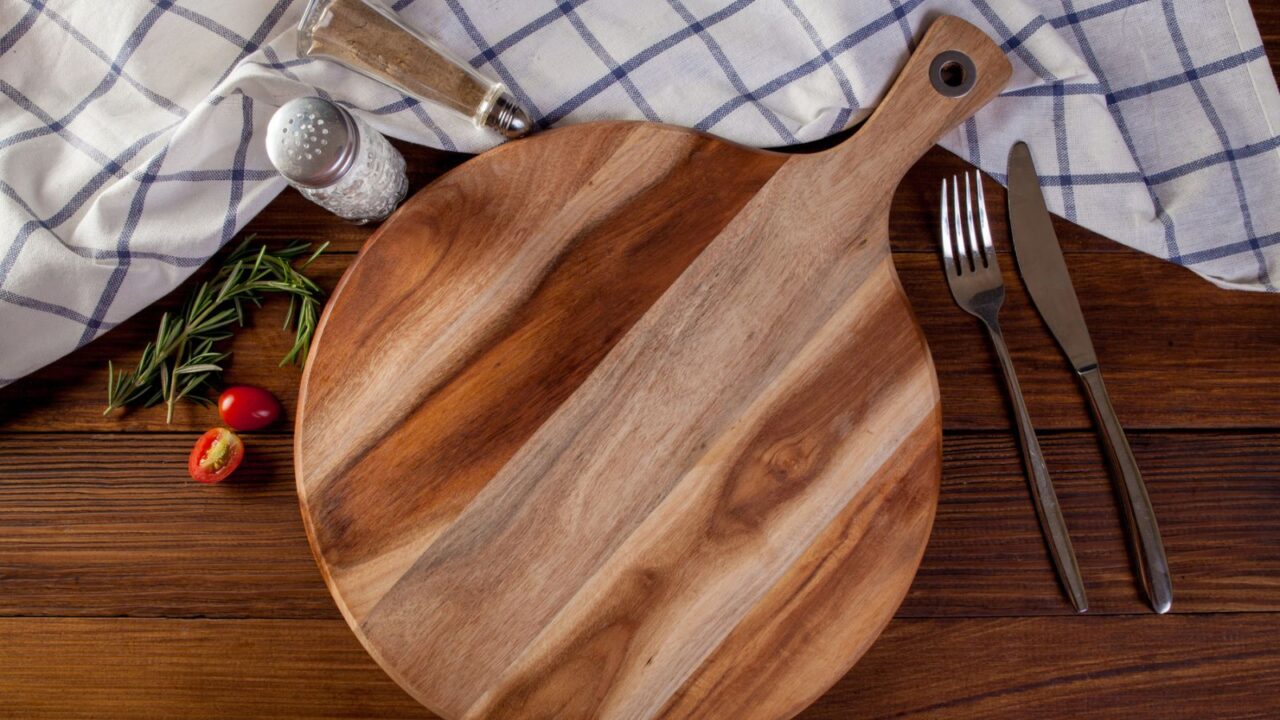 A wooden cutting board with a fork, knife, and a sprinkle of herbs beside fresh tomatoes.