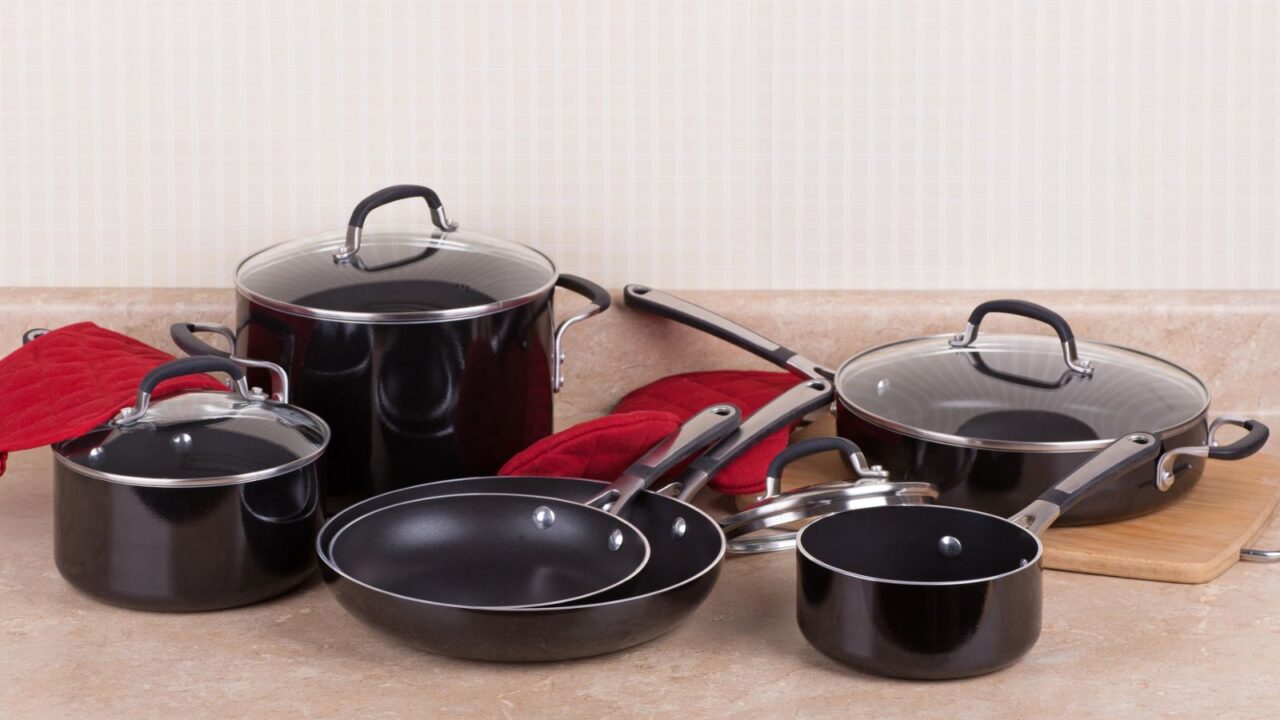 A collection of black cookware with glass lids and red pot holders arranged on a countertop.