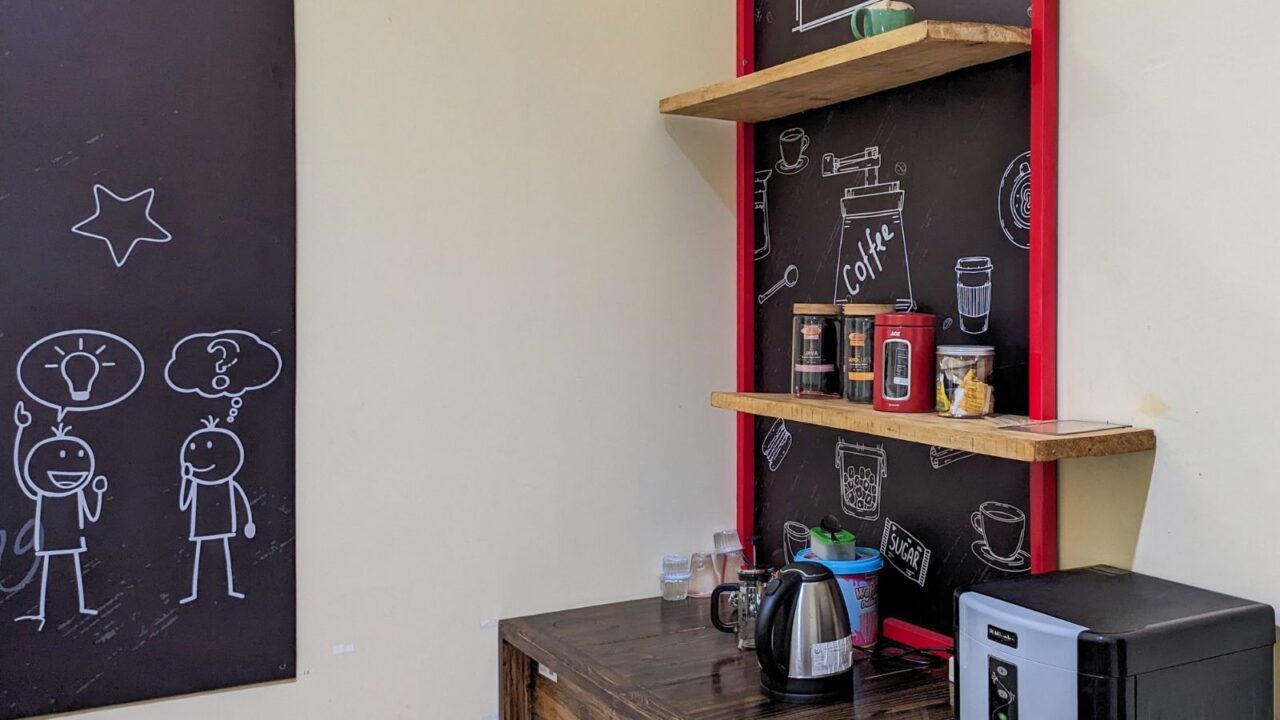 A blackboard wall with doodles and a wooden shelf holding various jars and a kettle.