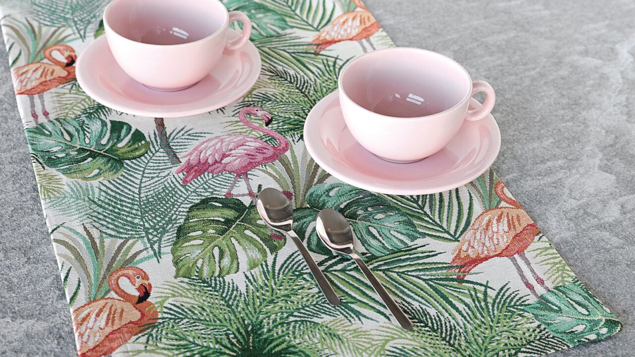 Two pink cups on saucers placed on a tropical leaf-patterned tablecloth.