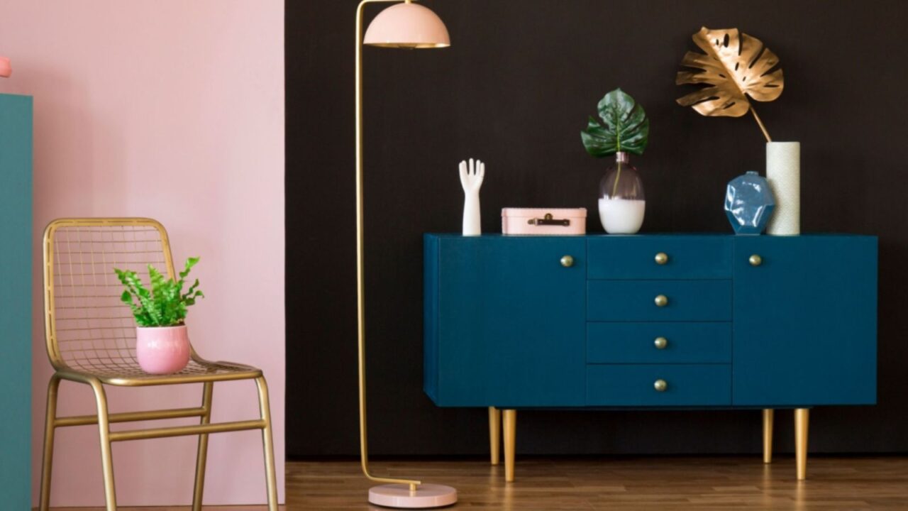 A colorful room featuring a teal cabinet, pink chair, and a decorative plant.