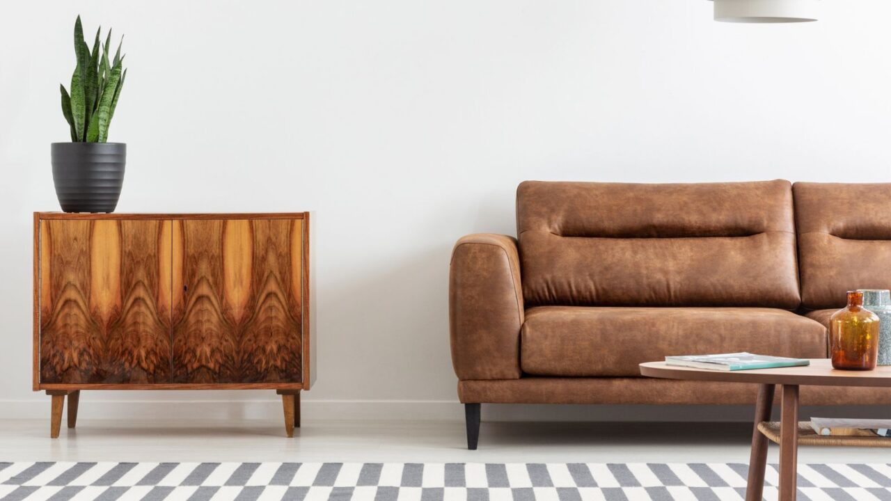 A mid-century modern living room featuring a brown leather sofa and a unique wooden cabinet, adorned with houseplants.