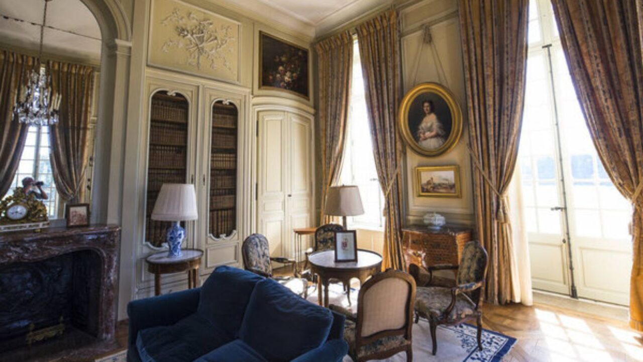 An opulent living room showcasing tall, luxurious curtains alongside bookshelves, a cozy fireplace, and refined artwork.