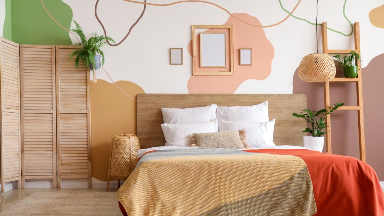 A warm-toned bedroom featuring a wooden bed, colorful bedding, and abstract wall art, with plants nearby.