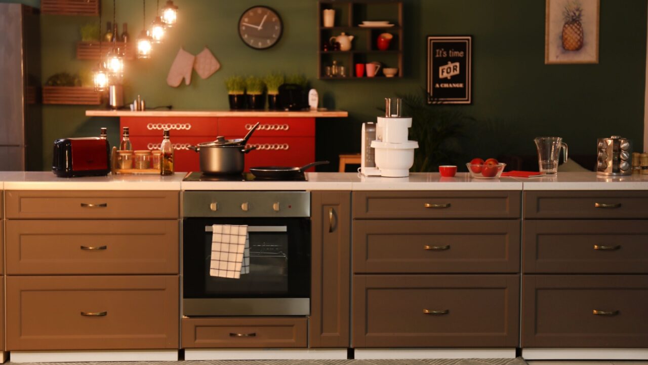 A modern kitchen with brown cabinets, various kitchen appliances, and a bowl of tomatoes on the countertop.