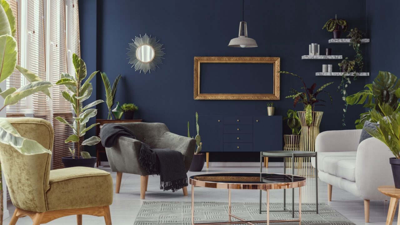 A modern living room with navy blue walls, featuring a variety of plants, mid-century modern furniture, and metallic decor elements.