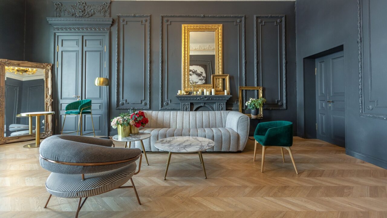 An elegant lounge area featuring a gray striped sofa, green accent chair, and a large gilded mirror reflecting the stylish decor against a dark wall.