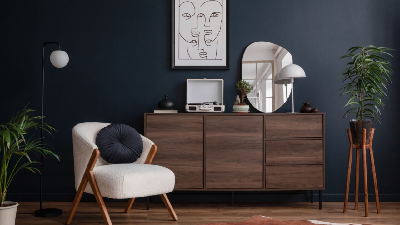 A chic arrangement of a plush armchair beside a stylish wooden sideboard and decorative items, framed by a rich blue wall and potted plants.