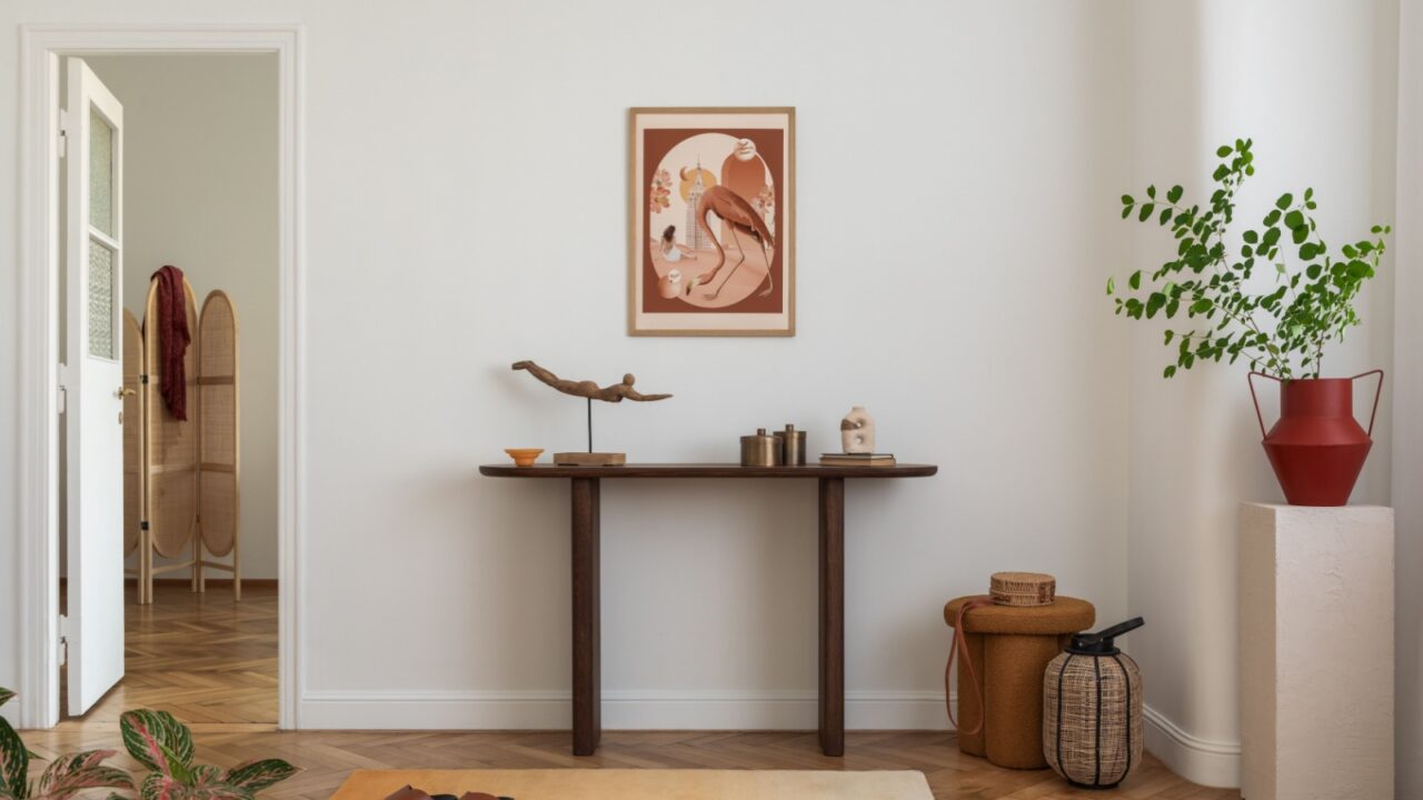 A console table with decor and a large green plant in a red pot against a white wall.