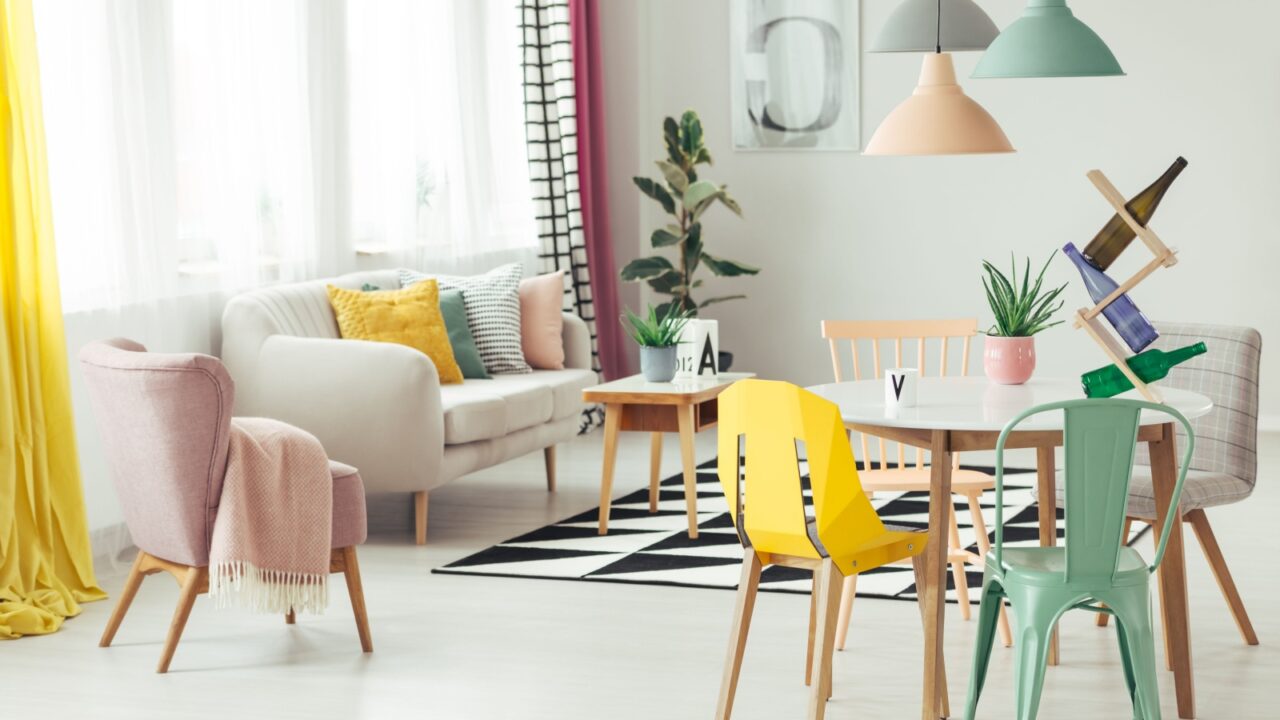 A hybrid dining and living room interior with white table, mix-and-match chairs, and pastel pendant lights.