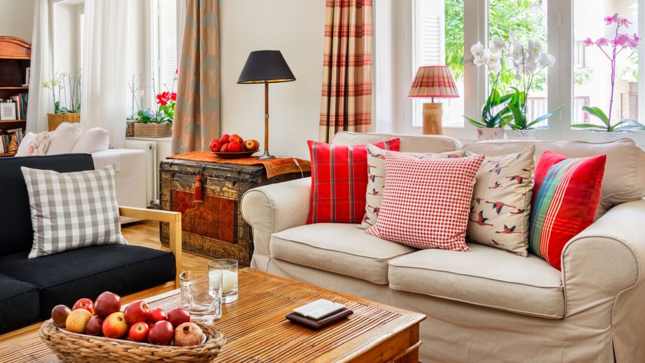 A cozy living room with a beige sofa adorned with colorful pillows, a wooden coffee table with a basket of apples, and a vintage trunk used as a side table.