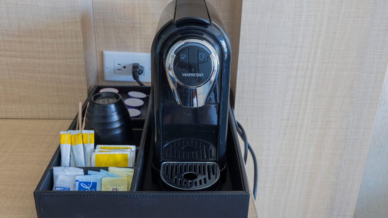 A coffee station with a coffee maker, cup, sugar, coffee pods, and creamers.