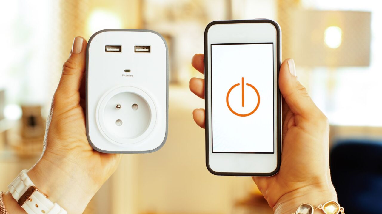 A woman holding a smartphone with smart home app and wifi smart plug.