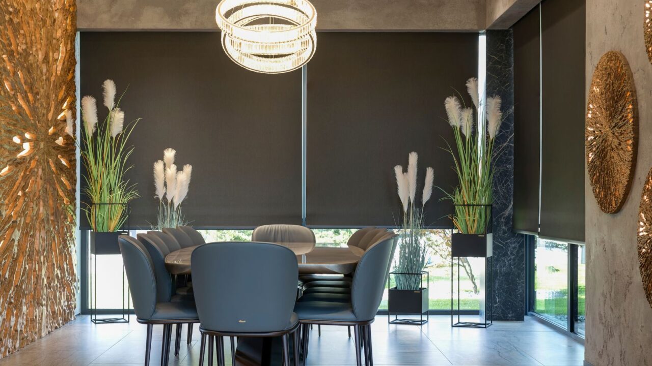 A dining room with table, chairs, plants, and automatic roller blinds.