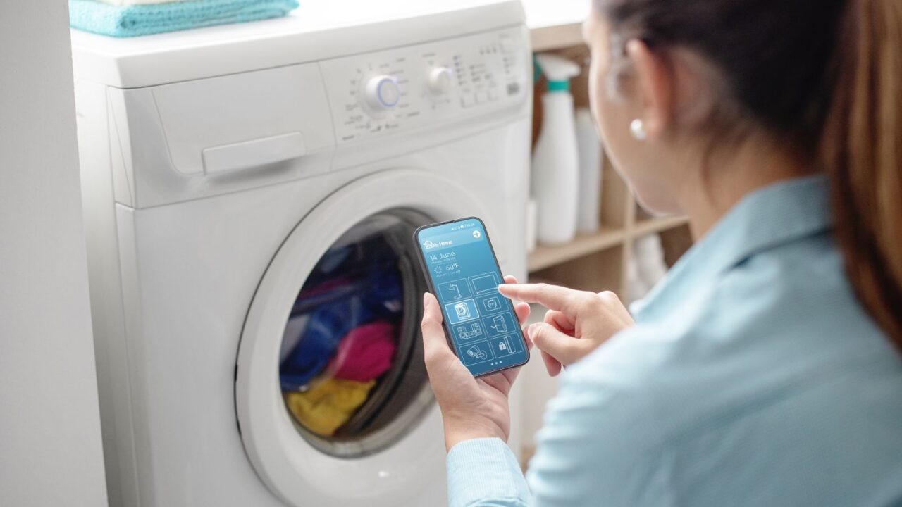 A woman operating a washing machine with her smartphone.