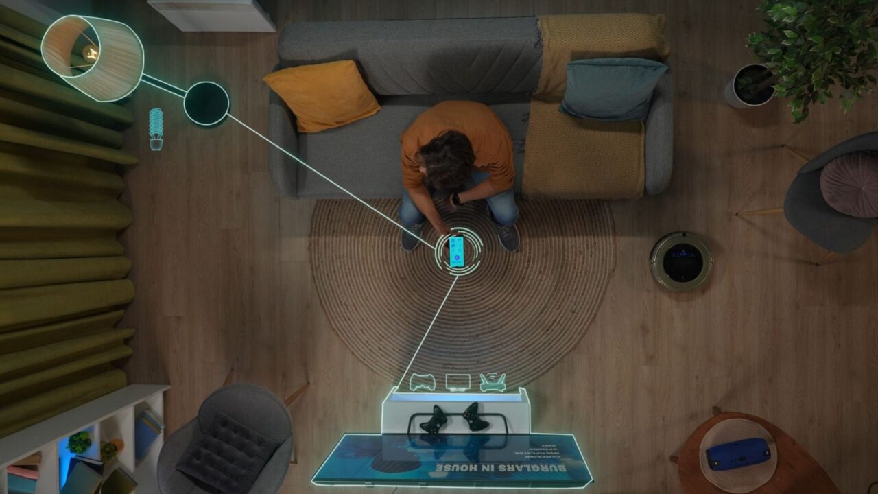 A man sitting on a couch in a living room and controlling the lamp and gaming TV with his smartphone.